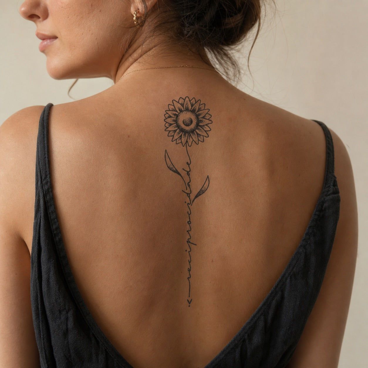Dotwork sunflower temporary tattoo with cursive script word on the stem, fine linework on white background.