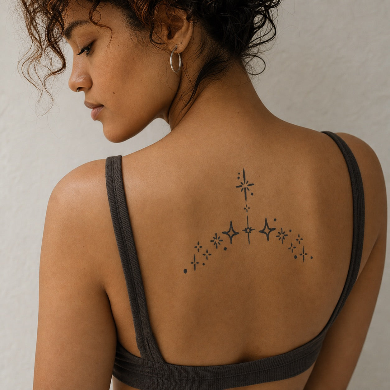 Scattered four-pointed star sparkle cluster temporary tattoo on white background, minimalist linework in diagonal arc arrangement.