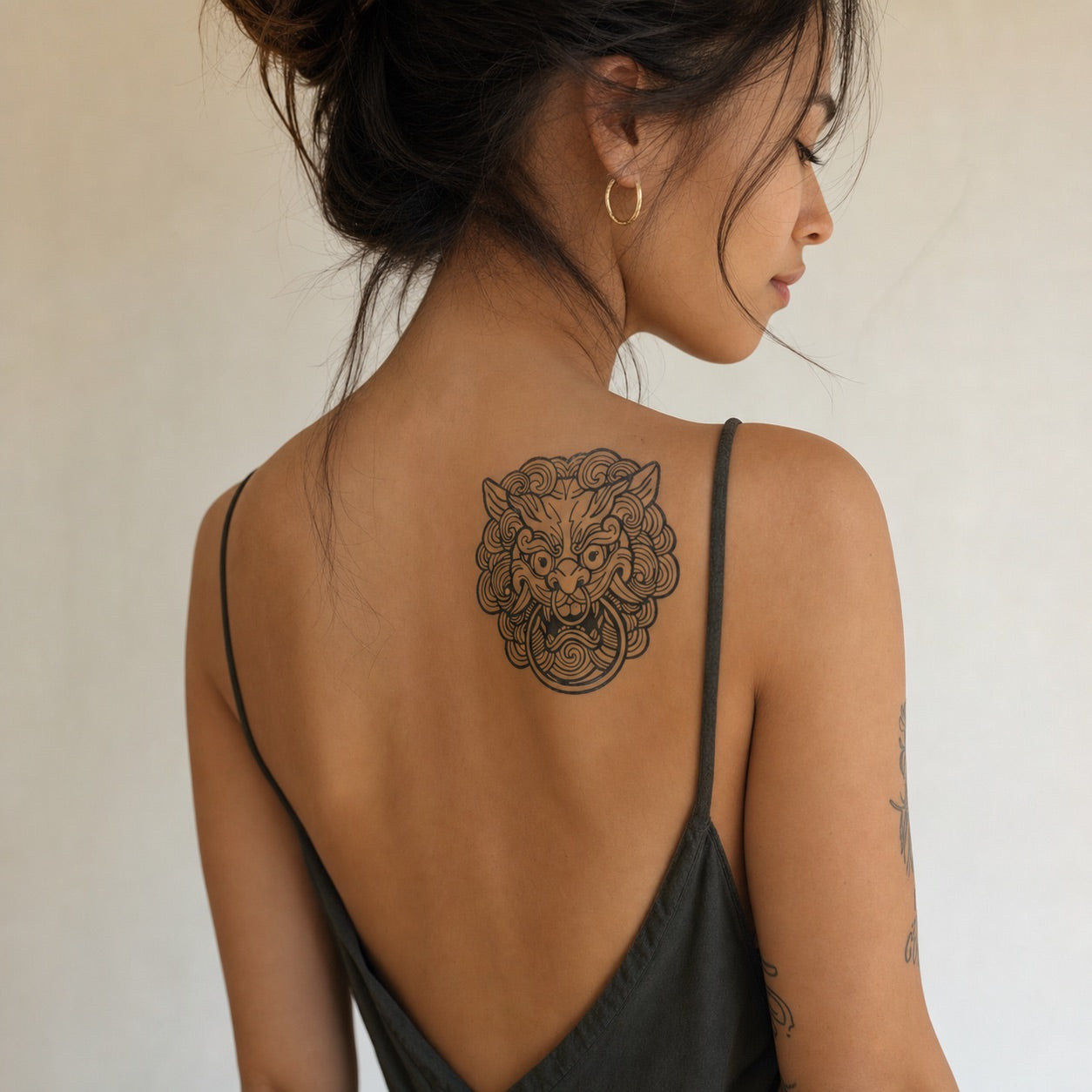 Chinese guardian lion foo dog temporary tattoo with swirling cloud mane and ring, bold linework on white background.