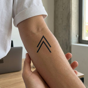 Double chevron arrow minimalist temporary tattoo, two stacked open triangles in dark linework on white background.