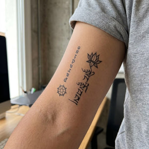 Lotus flower, Sanskrit script and dharma wheel vertical temporary tattoo with upside-down lettering, linework on white background.