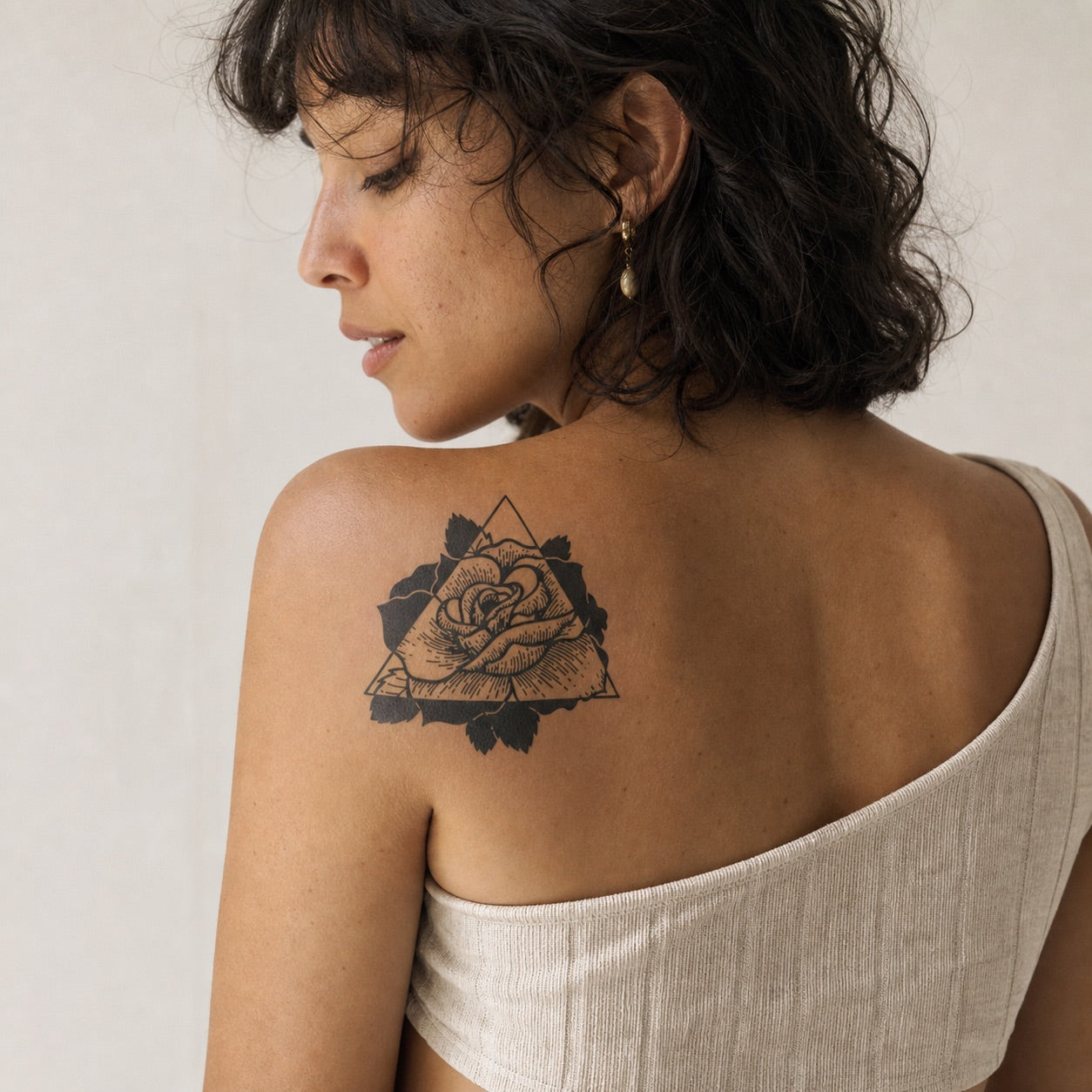 Geometric rose inside a triangle temporary tattoo with bold blackwork leaves, detailed linework on white background.