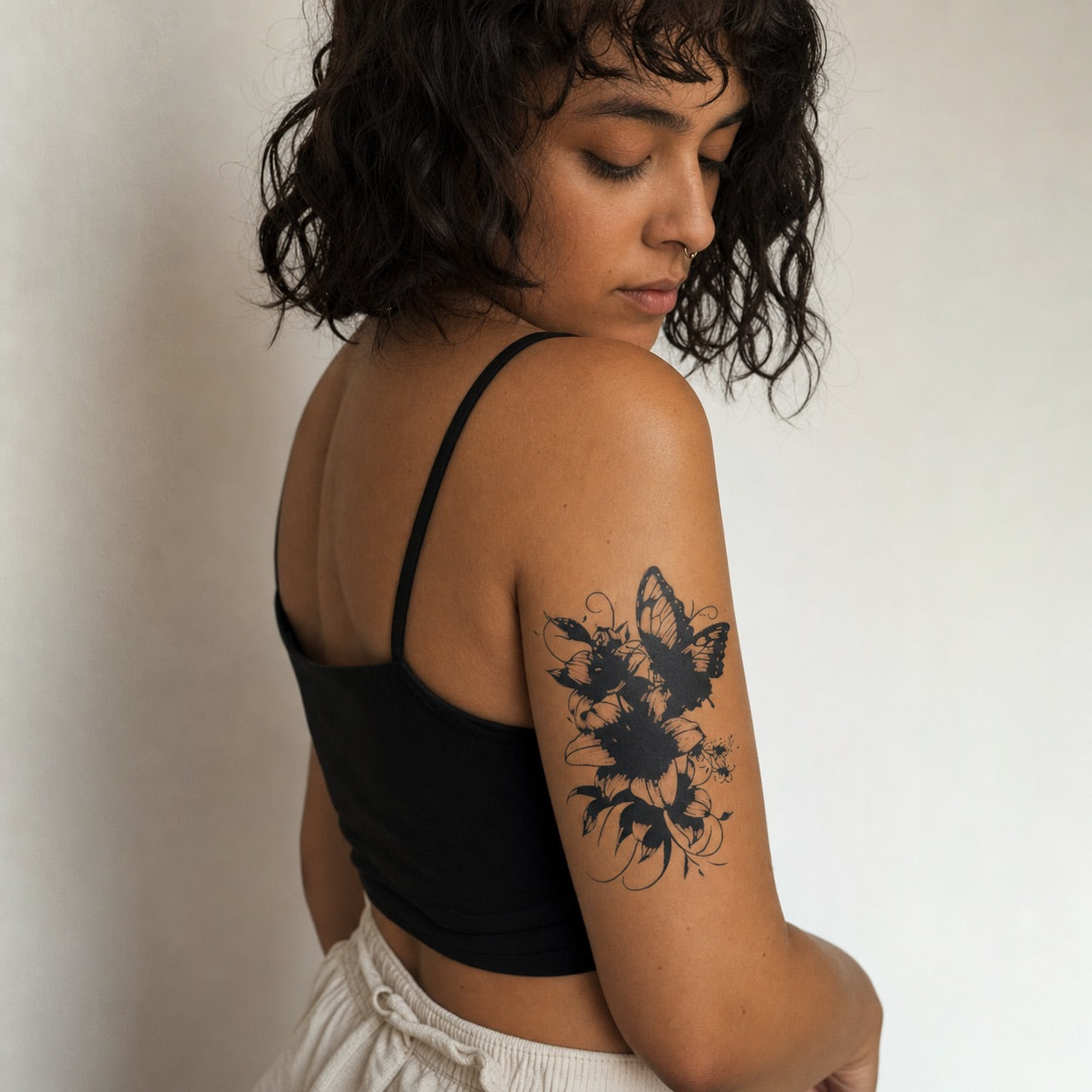 Bold blackwork butterfly perched on a sunflower temporary tattoo, detailed wings and curling vines on white background.